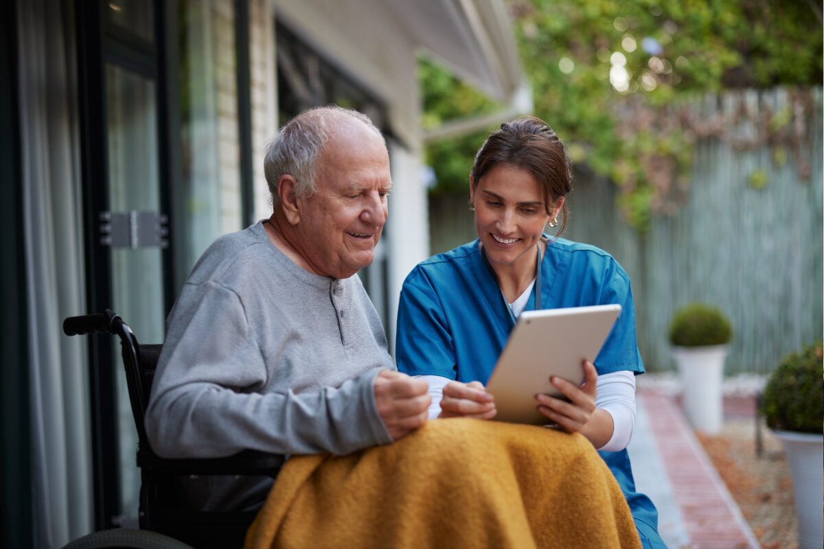 Caregiver showing tablet to man in wheelchair